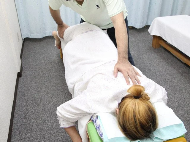 横向きで腰まわりの可動域を確認しながら整体している施術者の手元